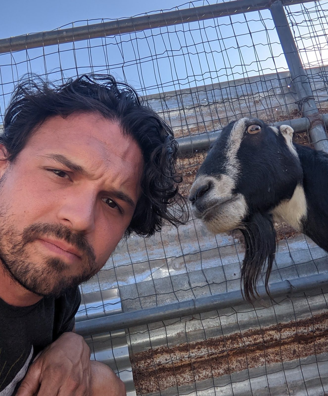Steven taking a selfie beside a black and white goat at a fence