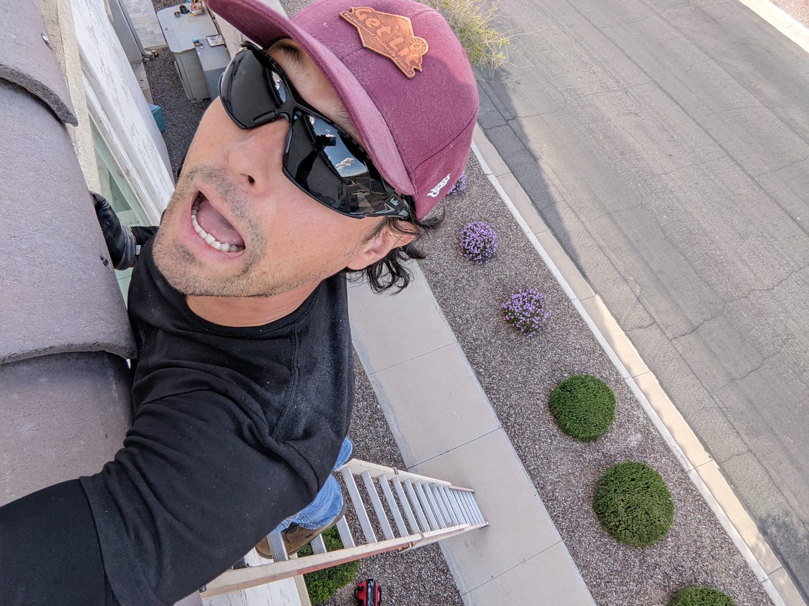 Steven at the top of a ladder against a roof edge, looking down at the street