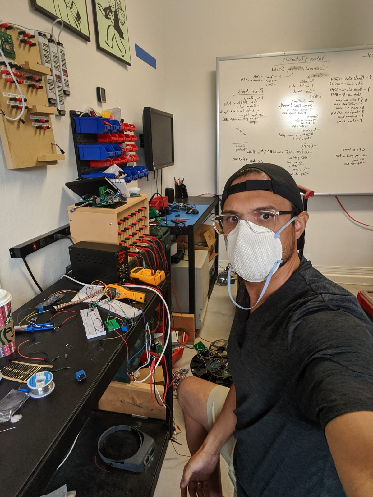 Steven at an electronics bench with breadboards, power supplies, and a whiteboard of notes